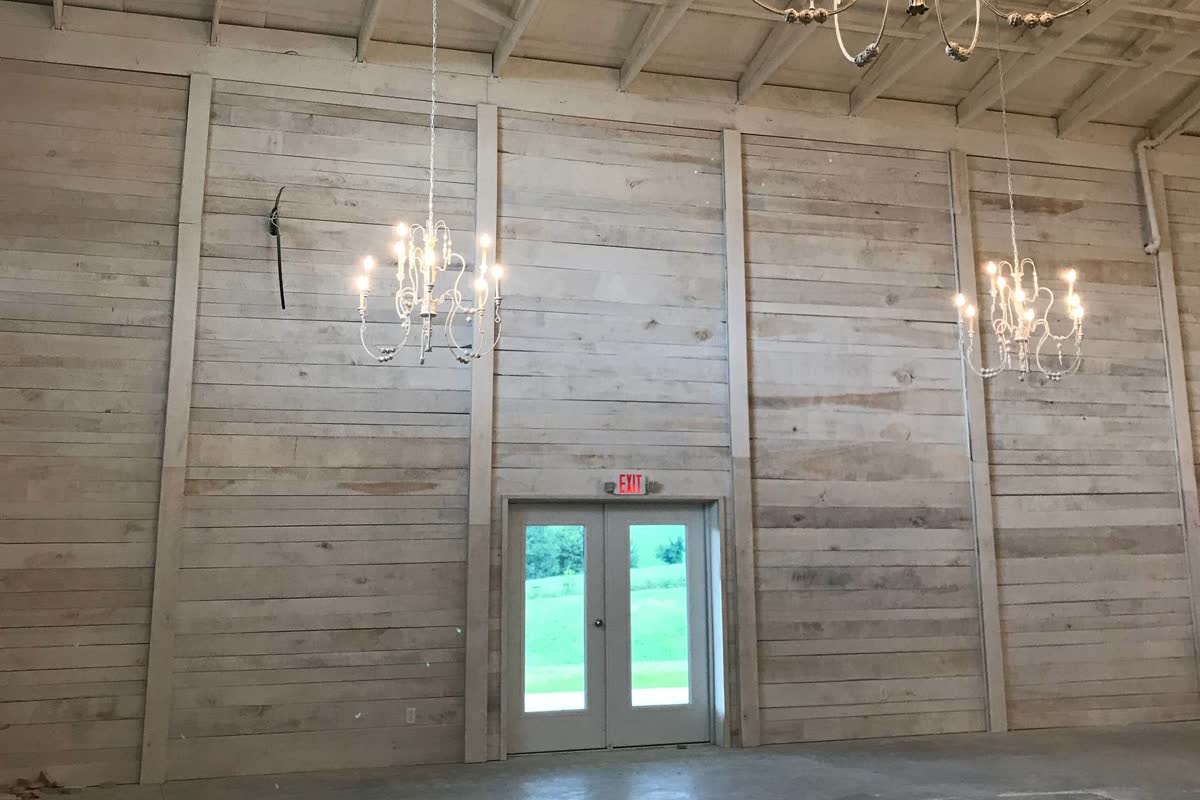 An event venue interior with whitewashed shiplap walls, exposed trusses, and chandeliers.