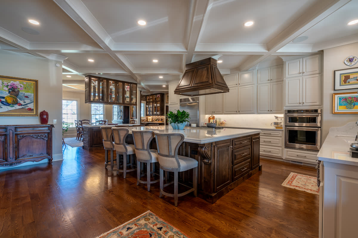 A renovated kitchen with a coffered ceiling, a carved wood island, and a custom range hood.
