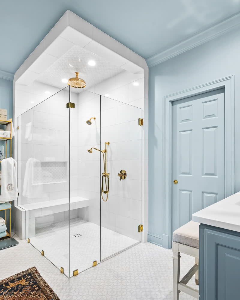 A bathroom with a glass shower enclosure, brass fittings, and pale blue walls.