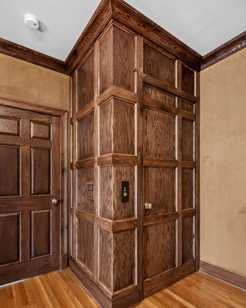 A custom oak-panelled elevator enclosure with raised-panel millwork and crown moulding.