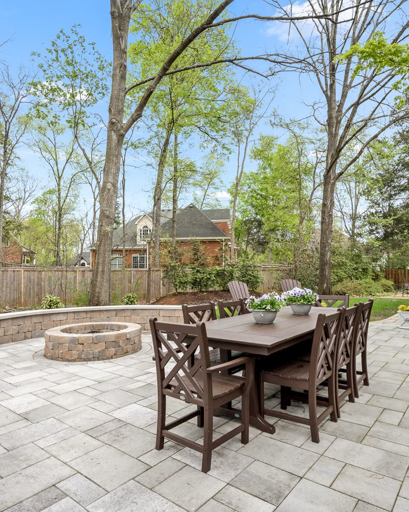 A stone patio with a built-in fire pit, curved seating wall, and outdoor dining table.