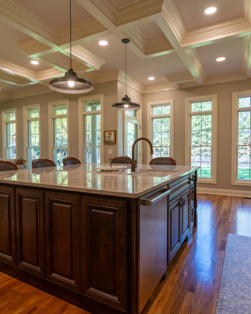 A kitchen with a coffered ceiling, a dark wood island, and a wall of windows.