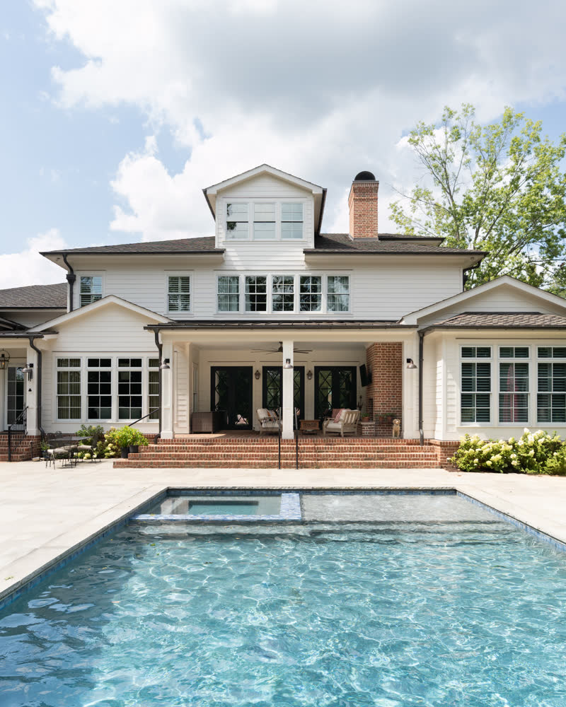 The rear elevation of a custom home with a covered porch overlooking a stone pool deck.